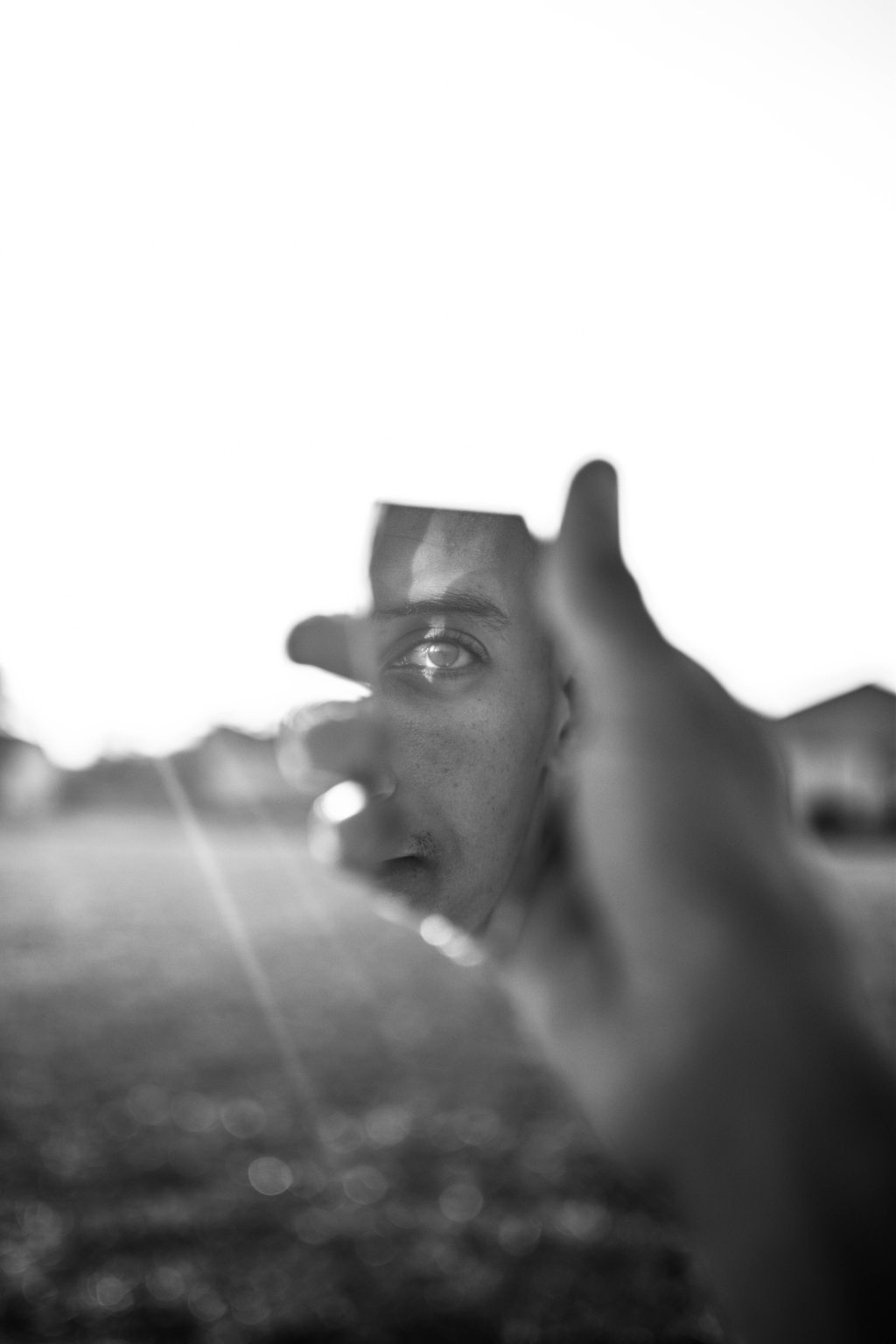 black and white photo of man holding a broken shard of mirror with his reflection in it