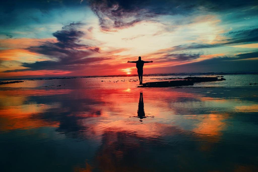photo of colorful sunset with silhouette of a man standing on water