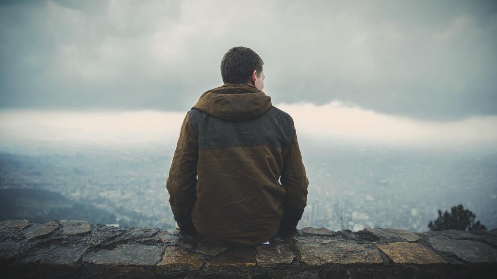 photograph of the back of a man sitting alone on a stone wall