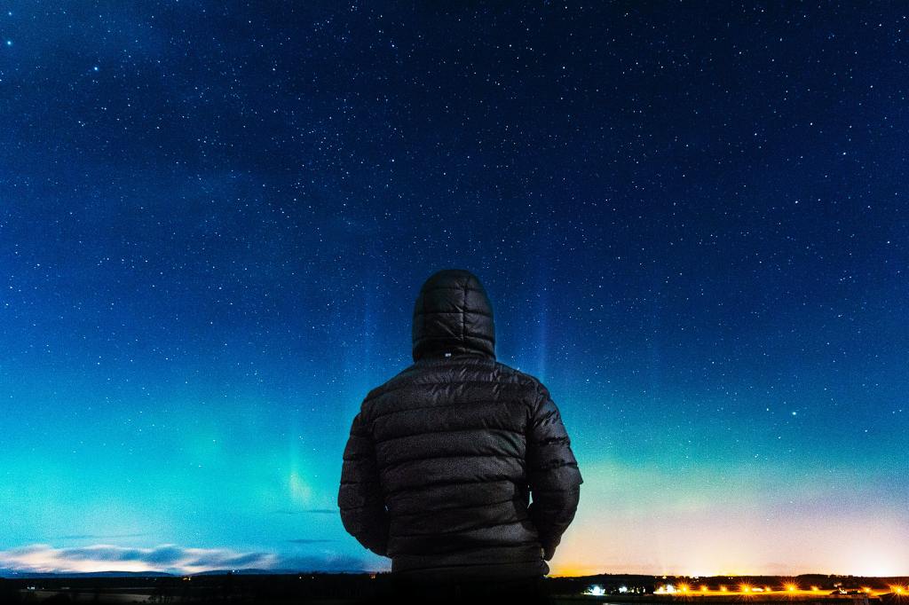 photograph of a man's back looking out into a vast night sky