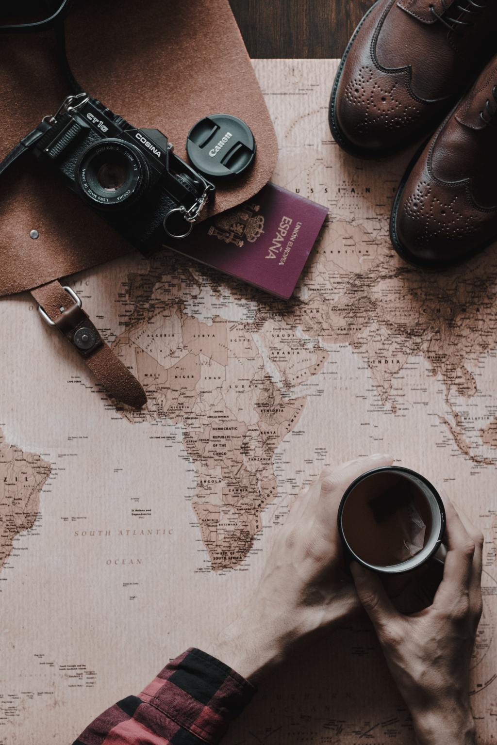 a map with camera, shoes and hands holding a coffee cup