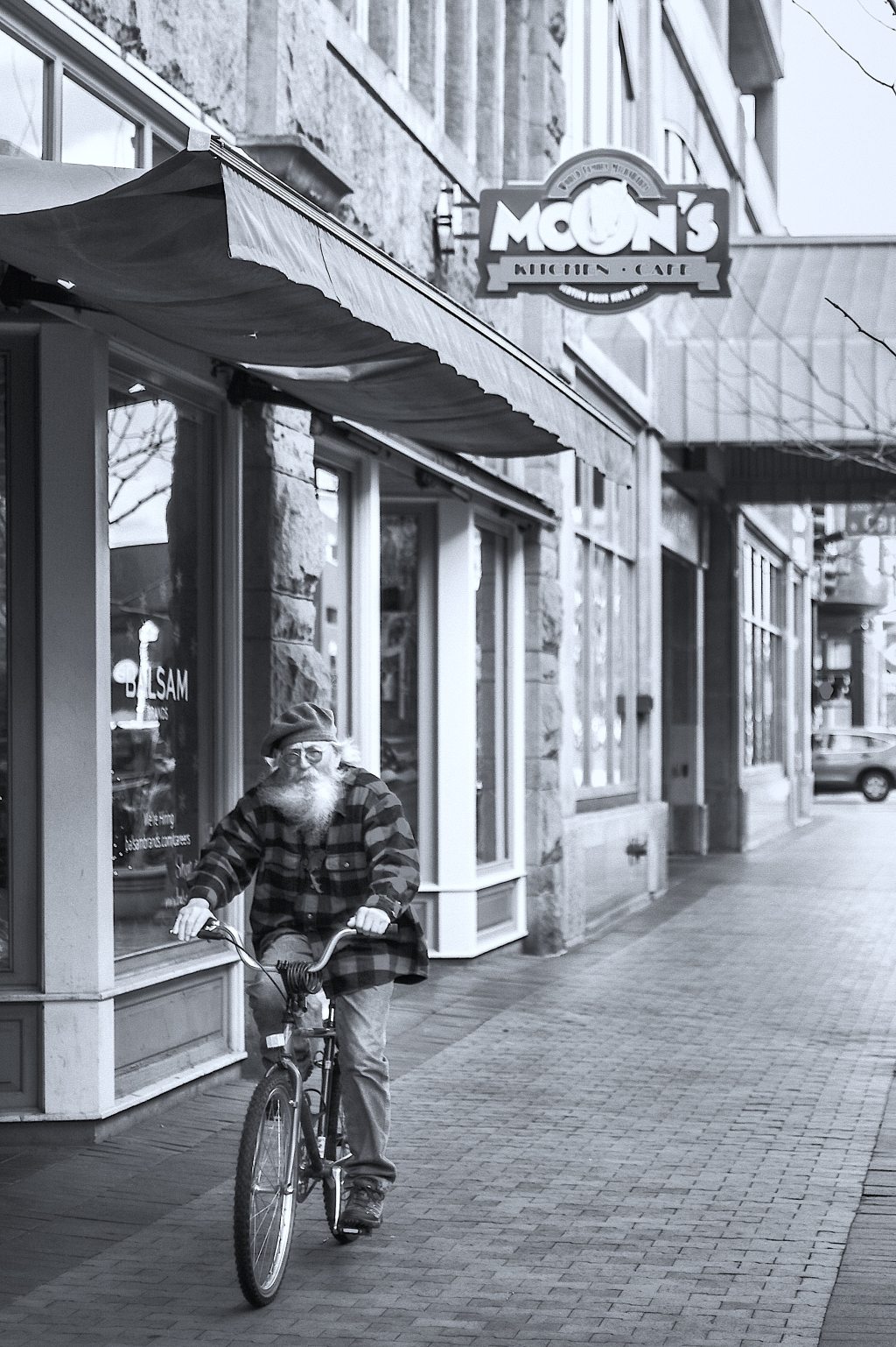 Bearded old man riding a bike on the sidewalk